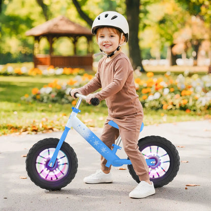 Toddler wearing safety helmet riding Frozen-themed toddler balance bike in a sunny park.